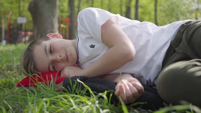 Boy lying on the grass in the park near the playground upset or tired after school on a warm spring weekend day