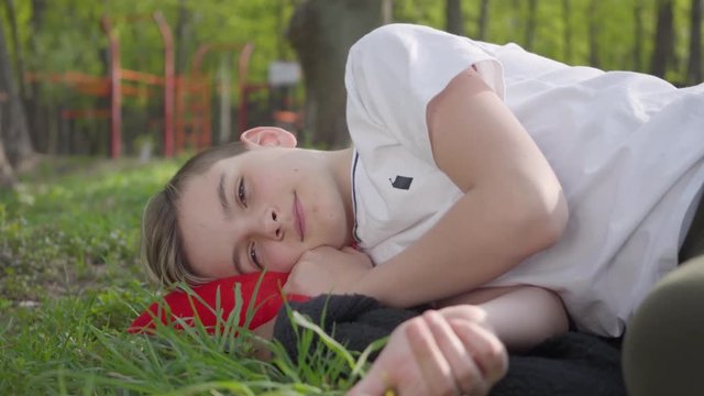 Portrait of a cute boy lying on green grass in spring park. Outdoor recreation.