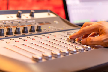 sound engineer fingers adjusting volume level fader on digital mixing console. music production,...