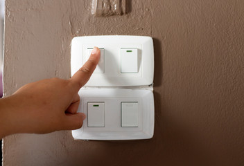 Close up hand turning on or off on grey light switch with wooden background. Copy space.