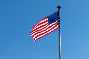 American flag, Stars & Stripes, waving in the wind, against a beautiful blue sky on a sunny summer day