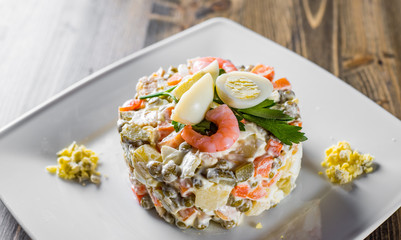 Olivier salad with shrimps, eggs and vegetables in a plate on wooden table