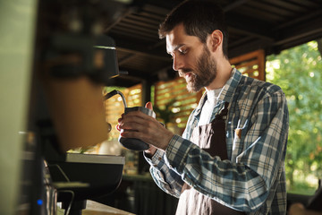 Image of attractive barista boy making coffee while working in cafe or coffeehouse outdoor