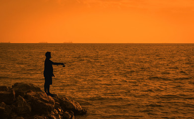 Fisher man fishing with spinning rod on a sea . Young men Fishing in the reservoir At sunset . Silhouette of a fisherman at sunset.