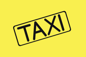 Word taxi in frame of black color cut out of black paper on yellow background. Top view. Concept of journey