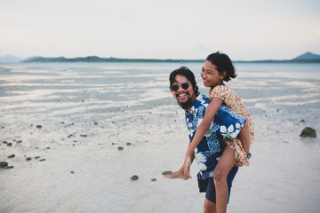 The daughter rides behind the father for a walk on the beach.