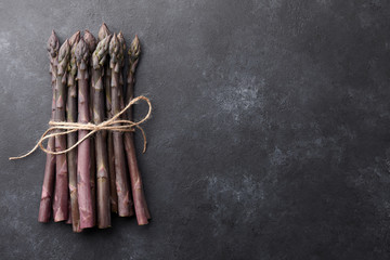 Bunch of fresh purple asparagus on black textured background, copy space