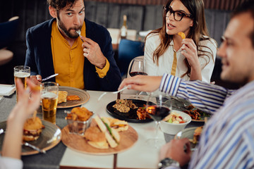 Multiethnic friends sitting at restaurant, drinking alcohol, chatting and having burgers for dinner.