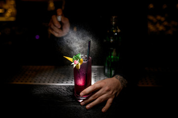 Bartender pours cocktail decorated with flower using sprayer