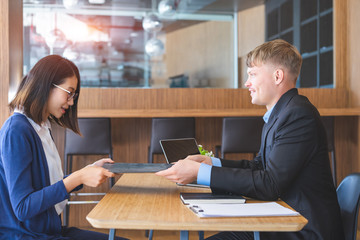 Human resources manager conducting job interview and receiving resume from young female candidate in modern office.