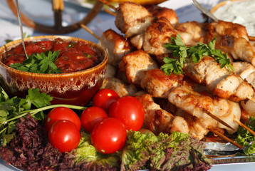 Table with cooked pork meat grilled shashlik on skewers with tomato sauce and fresh vegetables