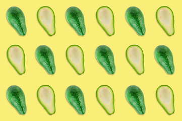 Rows of fresh wholes and halves of organic avocado without kernels in center of yellow table in kitchen or market. Top view. Cooking concept. Seamless pattern