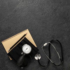 Blood pressure meter and stethoscope from above on dark stone background with notebook and pencil with space for notes, - Bilder