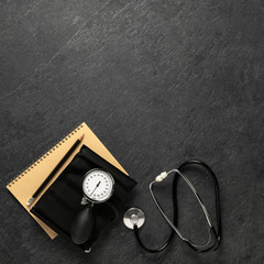 Blood pressure meter and stethoscope from above on dark stone background with notebook and pencil with space for notes, - Bilder
