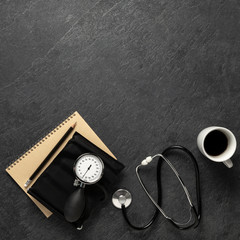 Blood pressure meter and stethoscope from above on dark stone background with notebook, pencil and a sup of coffee. space for text and notes, - Bilder