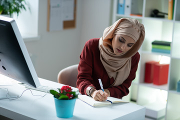 Beautiful Muslim woman writing into notebook while working