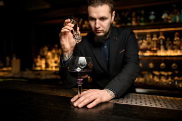 Bartender puts ice cube in alcohol cocktail