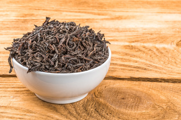 Dried tea is poured into a ceramic cup on a wooden plank table.