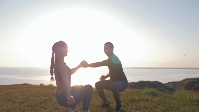 healthy lifestyle, couple athletic young woman and man holding hands and simultaneously crouching in sunlight at nature