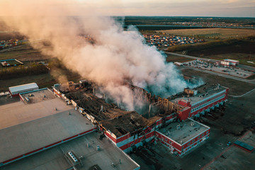 Aerial view of demolished burning industrial building by fire, huge smoke from broken roof, walls...