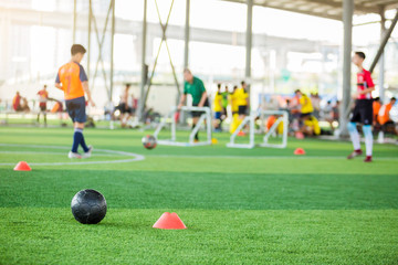 black football on green artificial turf with marker cone blurry soccer team training