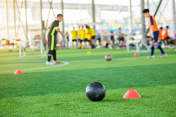 black football on green artificial turf with marker cone blurry soccer team training