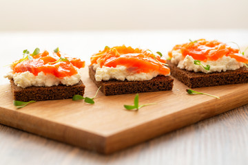 Canape with smoked salmon and cream cheese on wooden board. Selective focus