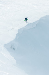 A snowboarder standing in front of the big cornice in the mountains, estimating the height for his jump