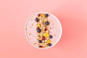 Smoothie bowl with pomegranates, blueberry and granola on a pink background. Tasty and healthy...