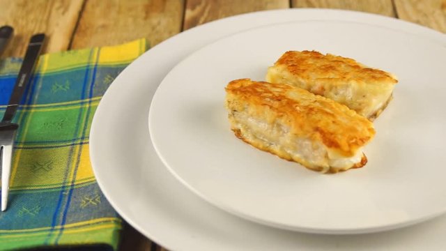 Deep-fried battered cod fillets, in a white plate on a wooden background. Close-up