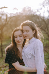 Portrait of two beautiful young sisters in the green spring garden, hugging in the field in the sunshine. Having fun together, positive emotions, bright colors. Copy space. Happy girlfriends at sunset