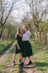 Portrait of two beautiful young sisters in the green spring garden, hugging in the field in the sunshine. Having fun together, positive emotions, bright colors. Copy space. Happy girlfriends at sunset