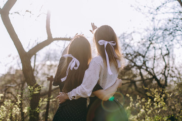 Portrait of two beautiful young sisters in the green spring garden, hugging in the field in the sunshine. Having fun together, positive emotions, bright colors. Copy space. Happy girlfriends at sunset
