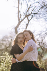 Portrait of two beautiful young sisters in the green spring garden, hugging in the field in the sunshine. Having fun together, positive emotions, bright colors. Copy space. Happy girlfriends at sunset