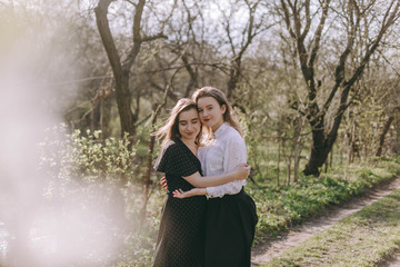 Fototapeta na wymiar Portrait of two beautiful young sisters in the green spring garden, hugging in the field in the sunshine. Having fun together, positive emotions, bright colors. Copy space. Happy girlfriends at sunset