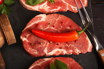 Raw pork meat steak with vegetables, peppers, tomato, salt, rosemary and spices cooking over stone table. Top view.