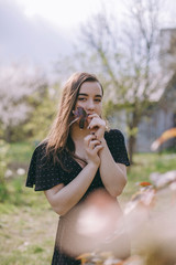 Portrait of a very beautiful sensual and brunette girl in a black dress, sincere smile, summer in the garden on a background of flowers, young student woman in the park in spring, sunny blooming day