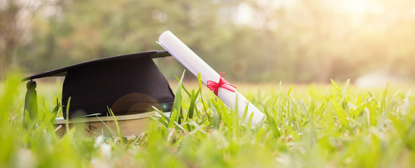 Closeup certificate paper and black cap on green grass spring time in the outdoor park. Education happy success achievement graduated celebrate graduate day concept panoramic background banner