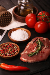 Raw pork meat steak with vegetables, peppers, tomato, salt, rosemary and spices cooking over stone table. Top view.