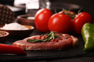 Raw pork meat steak with vegetables, peppers, tomato, salt, rosemary and spices cooking over stone table. Top view.