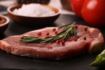 Raw pork meat steak with vegetables, peppers, tomato, salt, rosemary and spices cooking over stone table. Top view.
