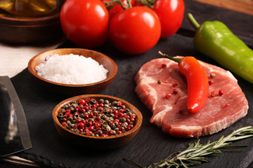 Raw pork meat steak with vegetables, peppers, tomato, salt, rosemary and spices cooking over stone table. Top view.