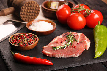 Raw pork meat steak with vegetables, peppers, tomato, salt, rosemary and spices cooking over stone table. Top view.