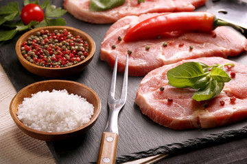 Raw pork meat steak with vegetables, peppers, tomato, salt, rosemary and spices cooking over stone table. Top view.