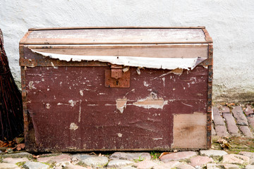 big damaged old wooden box, treasure case on pebbles, against white wall