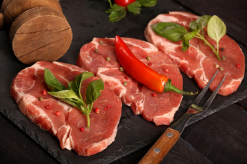 Raw pork meat steak with vegetables, peppers, tomato, salt, rosemary and spices cooking over stone table. Top view.