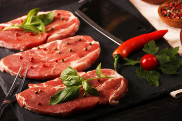 Raw pork meat steak with vegetables, peppers, tomato, salt, rosemary and spices cooking over stone table. Top view.