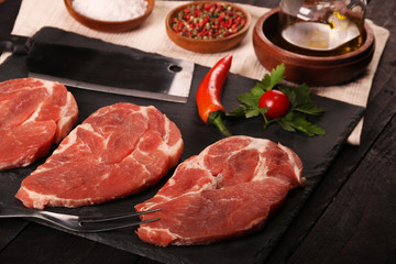 Raw pork meat steak with vegetables, peppers, tomato, salt, rosemary and spices cooking over stone table. Top view.