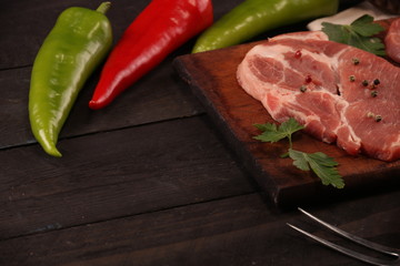 Raw pork meat steak with vegetables, peppers, tomato, salt, rosemary and spices cooking over stone table. Top view.