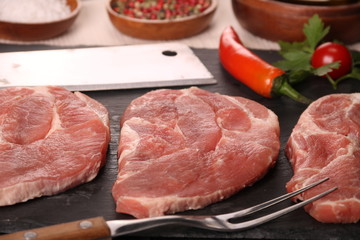 Raw pork meat steak with vegetables, peppers, tomato, salt, rosemary and spices cooking over stone table. Top view.